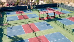 A tennis court with multiple courts, a covered seating area, and a fence.