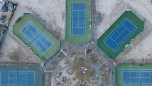 An aerial view of a sports complex with multiple tennis courts, pathways, and a central open area.