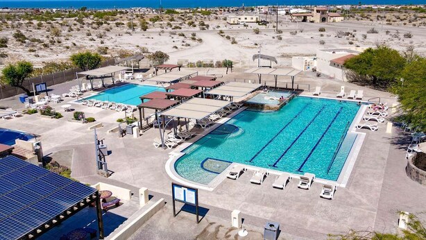 A large outdoor swimming pool with multiple lanes, sun loungers, and a covered area with a blue roof.