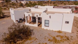 A modern white building with multiple rooms, outdoor seating, and a view of the surrounding desert landscape.