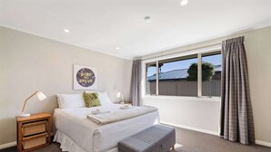 A bedroom with a large bed, bedside tables, a bench, a window with curtains, and a motivational poster on the wall. - Perfect Cromwell Family Getaway! (Cromwell)