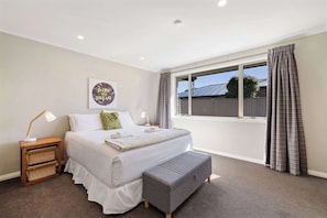 A bedroom with a large bed, bedside tables, a bench, a window with curtains, and a motivational poster on the wall.
