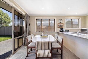A dining area with a round table, six chairs, a kitchen counter, and a sliding glass door leading to a patio.