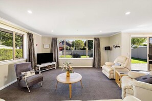 A living room with a flat-screen TV, two sofas, a coffee table, and large windows.