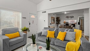 En moderne stue med en grå sofa, gule puder og et sofabord i glas.