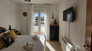 A bedroom with a bed, a flat-screen TV, a dresser, and a view of the outdoors through a sliding door. - Comfortable 2 bed apartment - La Torre Golf AA1911 (Murcia)