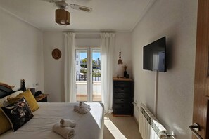 Une chambre à coucher comprenant un lit, un téléviseur à écran plat, une commode et une vue sur l’extérieur grâce à une porte coulissante.