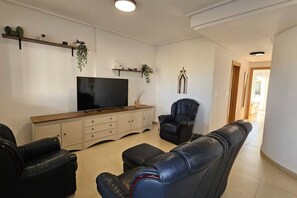 Una sala de estar con una televisión de pantalla plana, un sofá de cuero, un sillón de cuero y un mueble de madera con objetos decorativos.