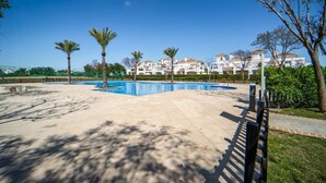 A swimming pool with a clear blue sky, palm trees, and a row of white buildings in the background. - Comfortable 2 bed apartment - La Torre Golf AA1911 (Murcia)