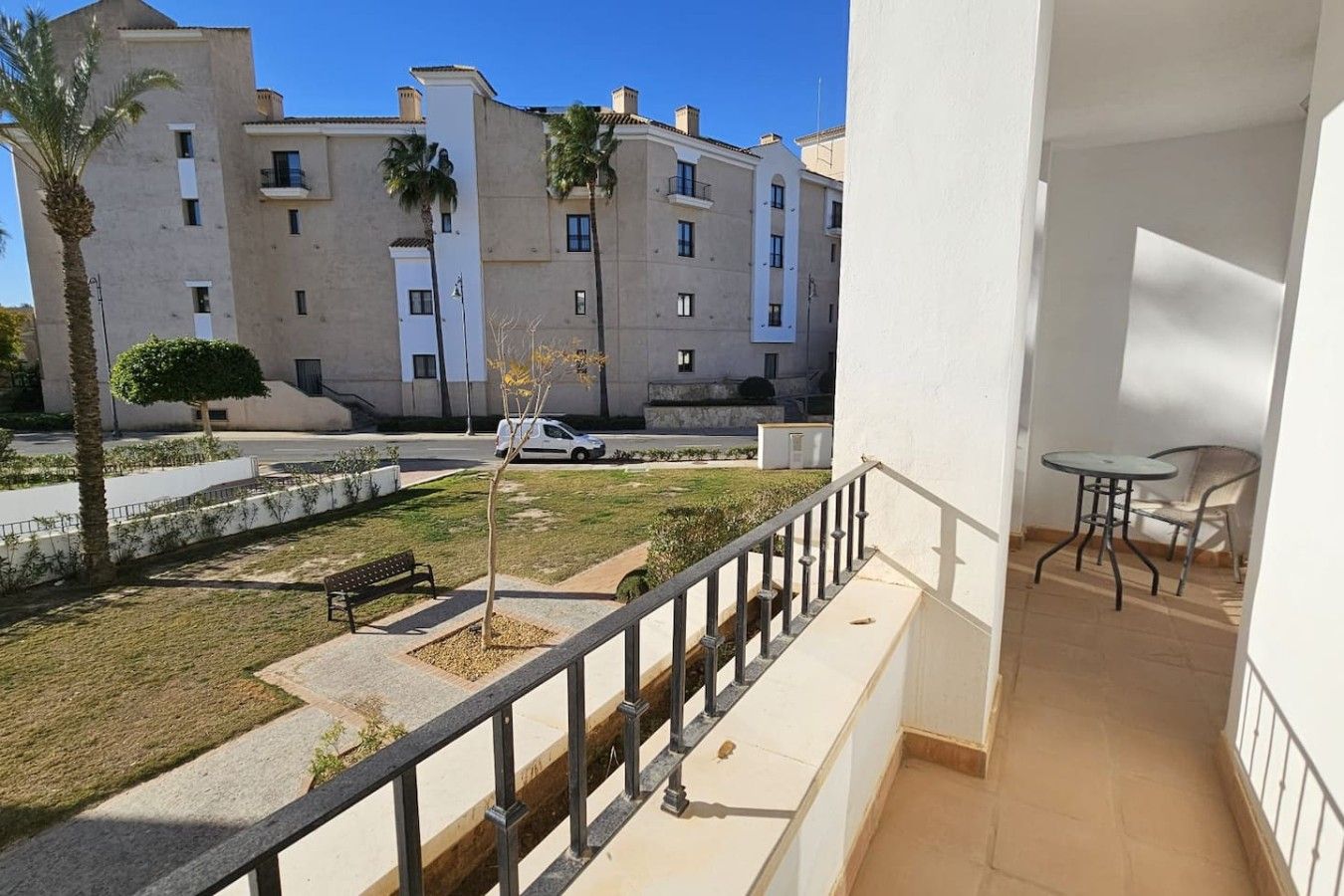 A balcony with a view of a courtyard, a bench, and a small table.