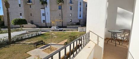A balcony with a view of a courtyard, a bench, and a small table.