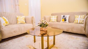 A living room with two beige sofas, a glass coffee table, and a vase of flowers. - Havana Cottages-Telaviv (Nakuru)