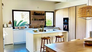 A modern kitchen with a central island, wooden cabinets, and a large window providing natural light. - CASA LECCIA, Luxurious villa with swimming pool 5' drive from ST FLORENT (Patrimonio)