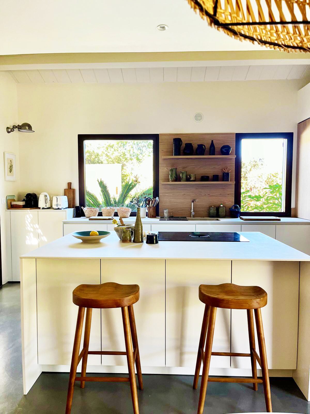 Une cuisine moderne dotée d’un grand îlot central, de tabourets en bois et d’une fenêtre donnant sur un paysage verdoyant.