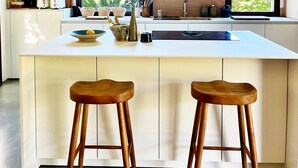 A modern kitchen with a large island, wooden stools, and a window with a view of greenery. - CASA LECCIA, Luxurious villa with swimming pool 5' drive from ST FLORENT (Patrimonio)