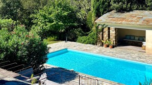 A swimming pool with a stone deck, surrounded by lush greenery and a mountain in the background. - CASA LECCIA, Luxurious villa with swimming pool 5' drive from ST FLORENT (Patrimonio)