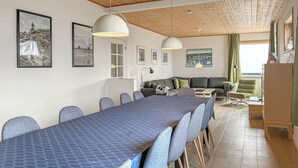 A modern dining area with a long table and chairs, a sofa, and a green armchair.