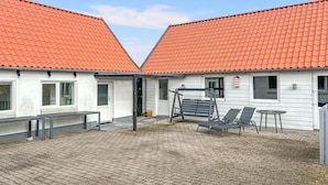 A building with two red-tiled roofs, a paved patio with outdoor furniture, and a small table.