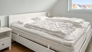 A bedroom with two beds, a nightstand, and a window with a view of houses.