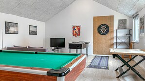 A room with a pool table, a dartboard, a television, and a foosball table.