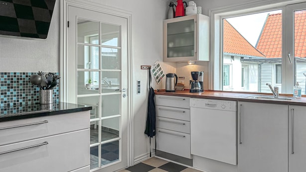 A modern kitchen with white cabinets, a Bosch dishwasher, a coffee maker, and a window with a view of a red-roofed building.