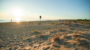 Een zandstrand met voetafdrukken, een redershut en een persoon die loopt.