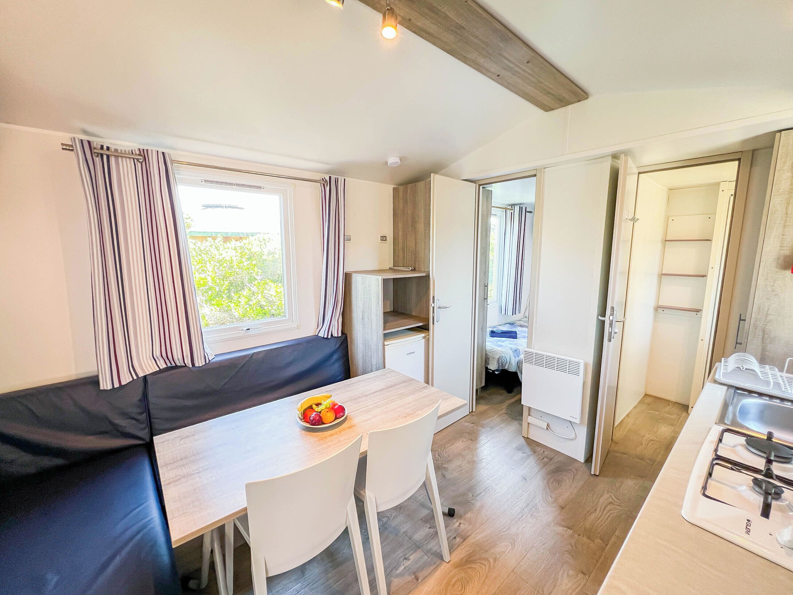 A compact kitchenette with a gas stove, a small dining table with chairs, and a bench with a fruit bowl.