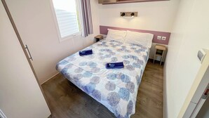 Een slaapkamer met een bed, een raam met gordijnen, een nachtkastje en een wandplank.