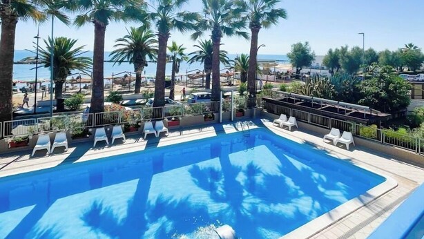 Une piscine entourée de chaises longues, de palmiers et surplombée d’un ciel dégagé.