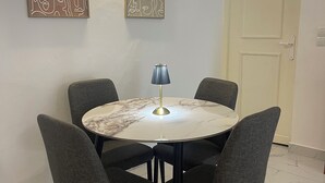 Una zona de menjador amb una taula rodona i quatre cadires grises, dues obres d'art penjades a la paret, una porta i un sòl amb disseny de marbre.