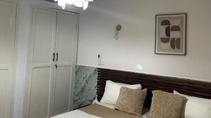Un dormitori amb un llit, un armari, un panell de capçal, una làmpada fixa a la paret i una fotografia emmarcada.