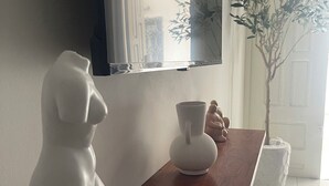 Una taula consola de fusta, una escultura de bust blanc, un vas de flors blanc i una petita planta en test.