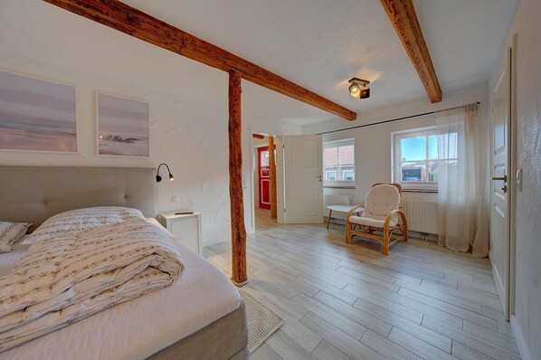 A bedroom with a bed, a chair, a nightstand, and a window with curtains.