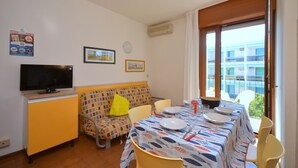 A dining area with a table set for two, a sofa, a television, and a window with a view of buildings. - Sunny sea view house in a central area (Bibione)