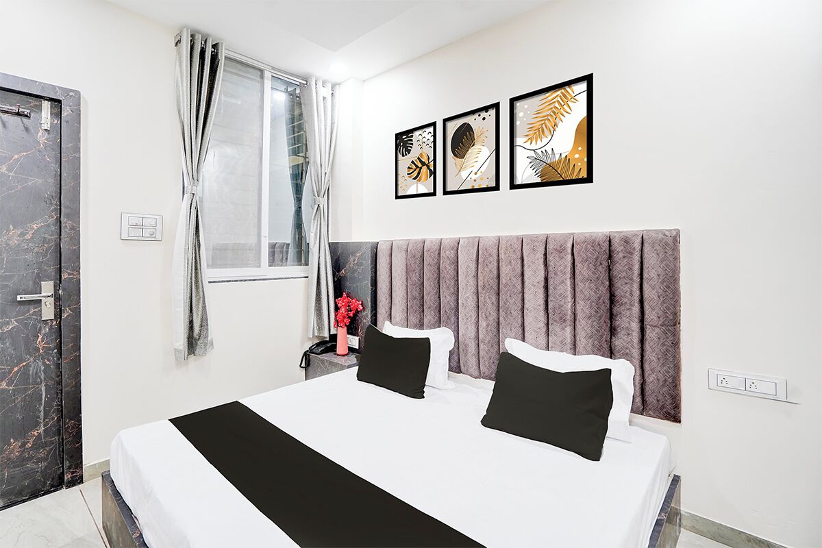 A hotel room with a large bed, a headboard, a window with curtains, and three framed artworks on the wall.