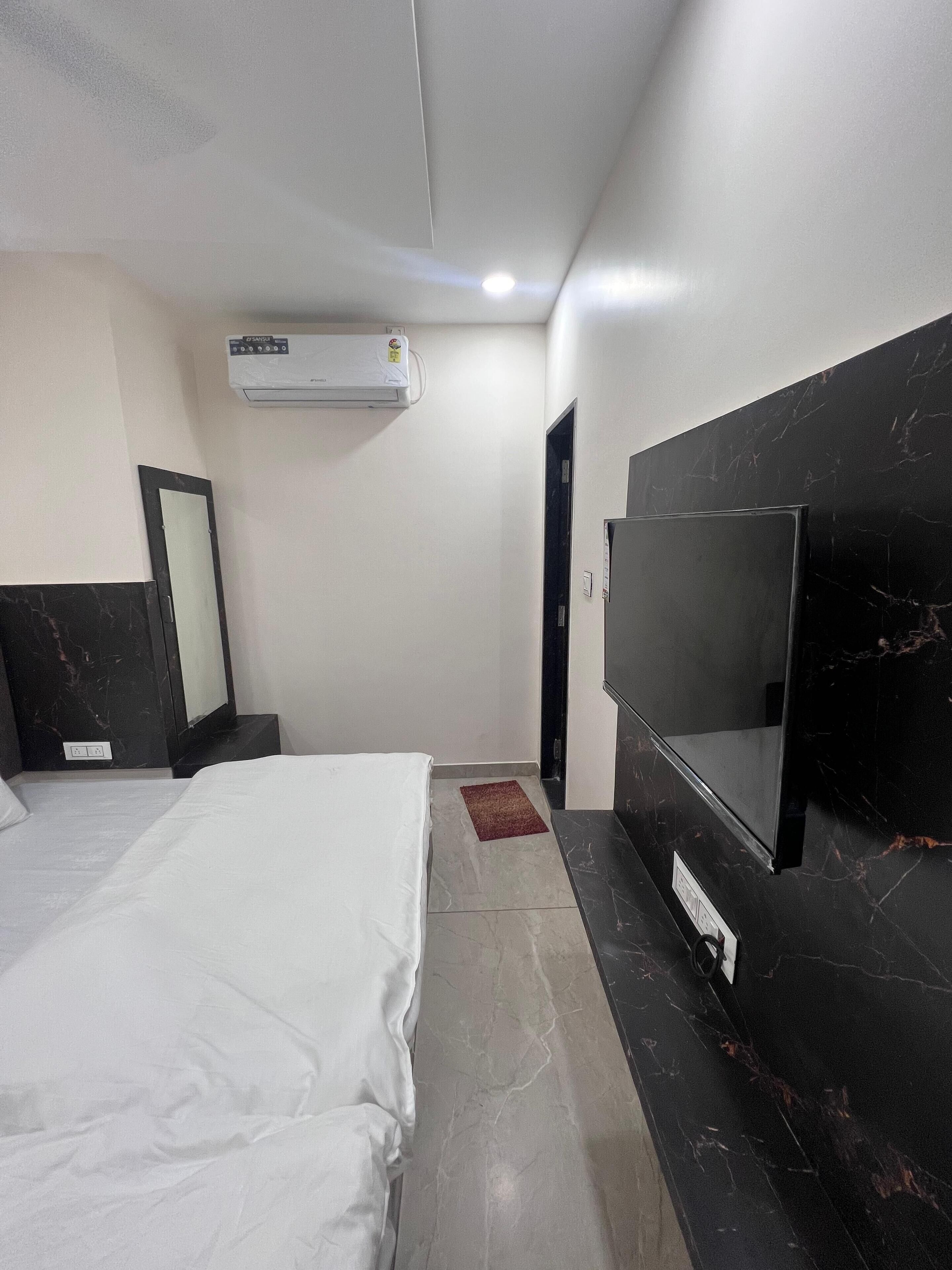 A hotel room with a bed, a TV, a mirror, and an air conditioning unit.