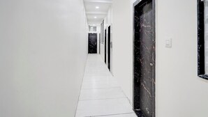 Ένας μακρύς, στενός διάδρομος με λευκούς τοίχους και πλακάκια στο δάπεδο, που οδηγεί σε μια πόρτα με επένδυση από μαύρο μάρμαρο.