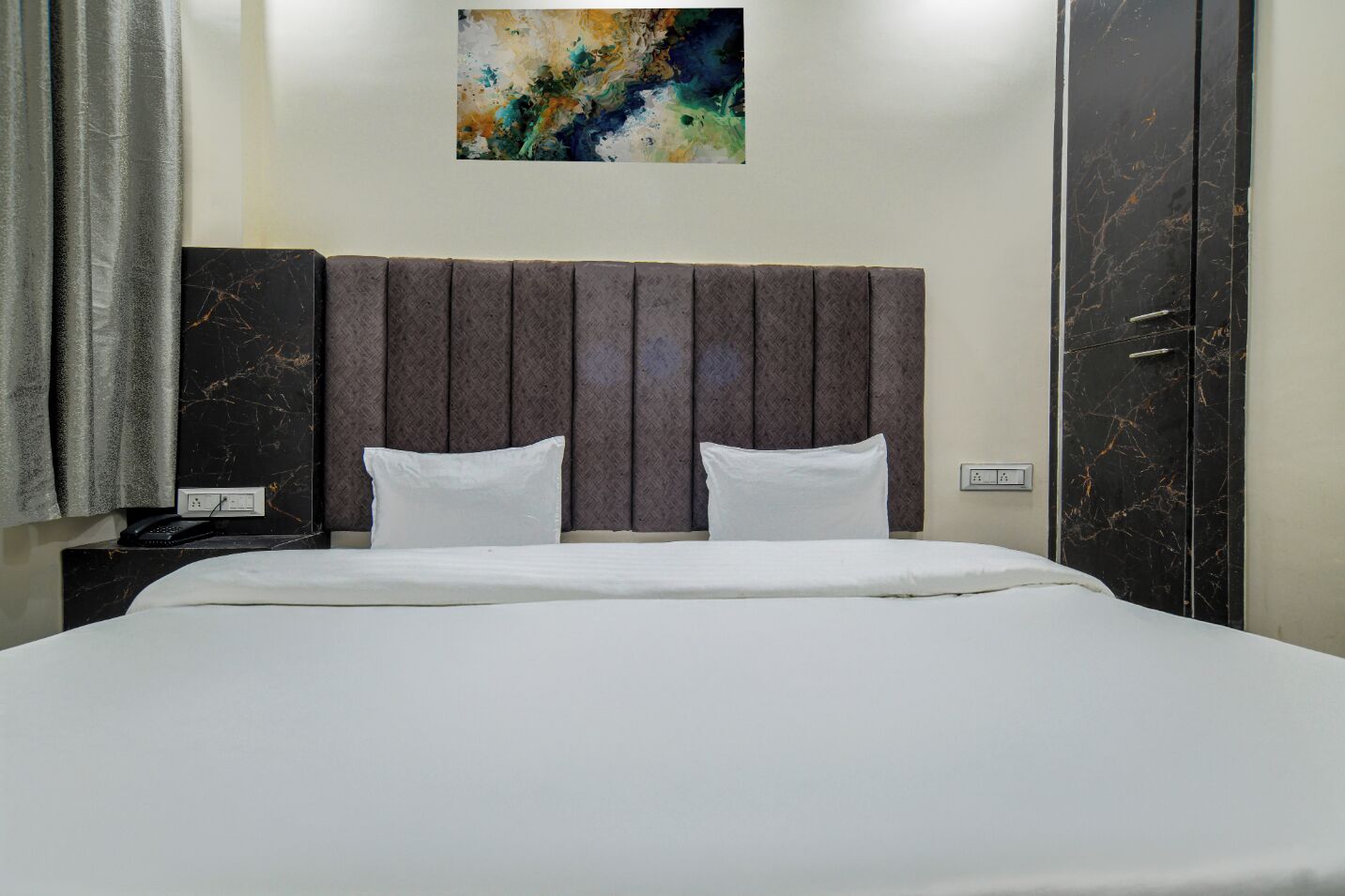 Quarto de hotel com uma cama grande, cabeceira, mesa de cabeceira, telefone e um quadro na parede.