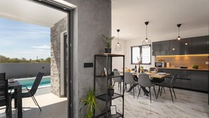 A modern kitchen with dark cabinets, a wooden countertop, and a dining area with a table and chairs. - Awesome home in Jursici (Jursici)
