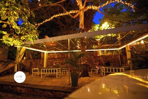 An outdoor seating area with tables and chairs, a stone wall, and a tree with string lights.