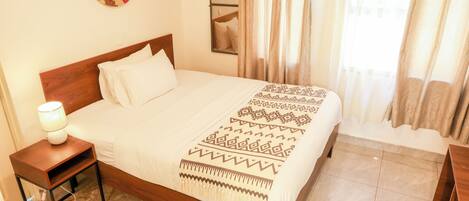 A neatly made bed with a patterned bedspread, a bedside table with a lamp, and a mirror on the wall.