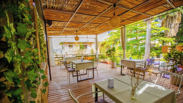An outdoor patio with wooden flooring, tables, and chairs, surrounded by greenery and plants. - Kalih Villa (Kigali)