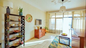 A living room with a wooden shelf, a television, a patterned rug, and a ceiling with decorative molding. - Kalih Villa (Kigali)