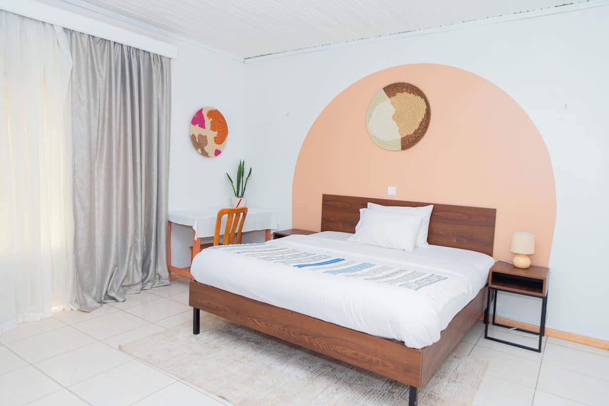 Une chambre à coucher bien rangée, avec un lit en bois, une table de chevet, une chaise et un objet décoratif fixé au mur.