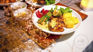 A table with various dishes, including a plate with grilled chicken, vegetables, and potatoes. - Kalih Villa (Kigali)