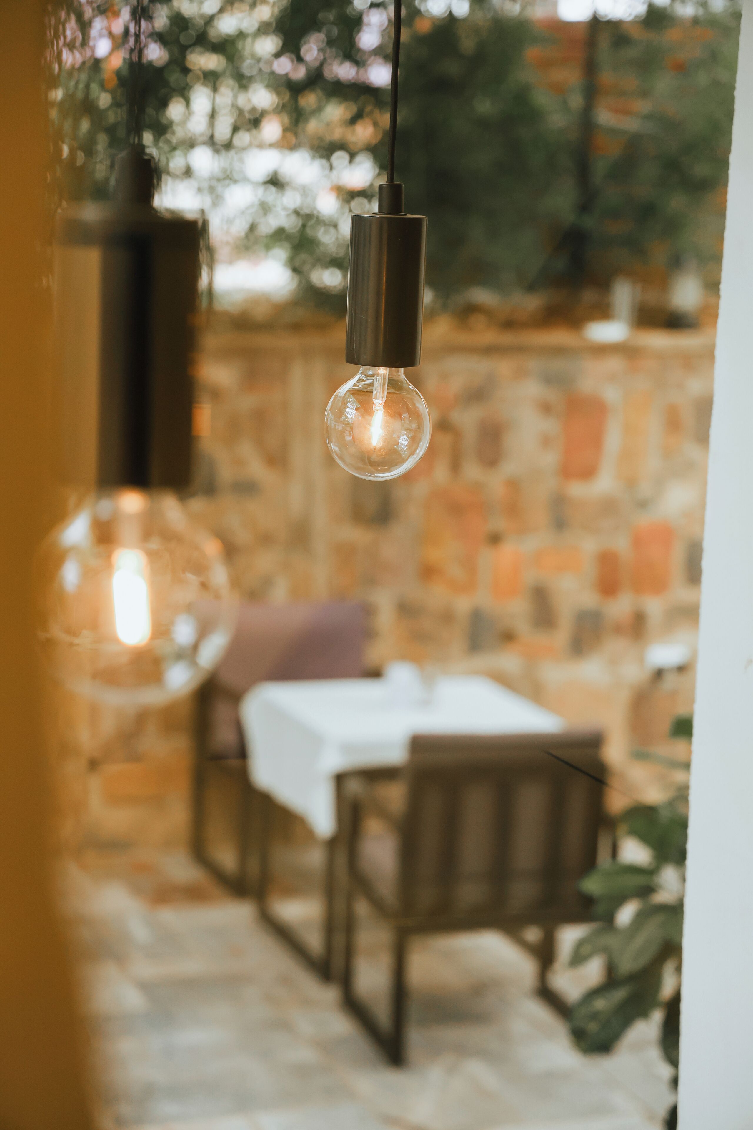 A dining area with a stone wall, a table with a white tablecloth, and hanging pendant lights.