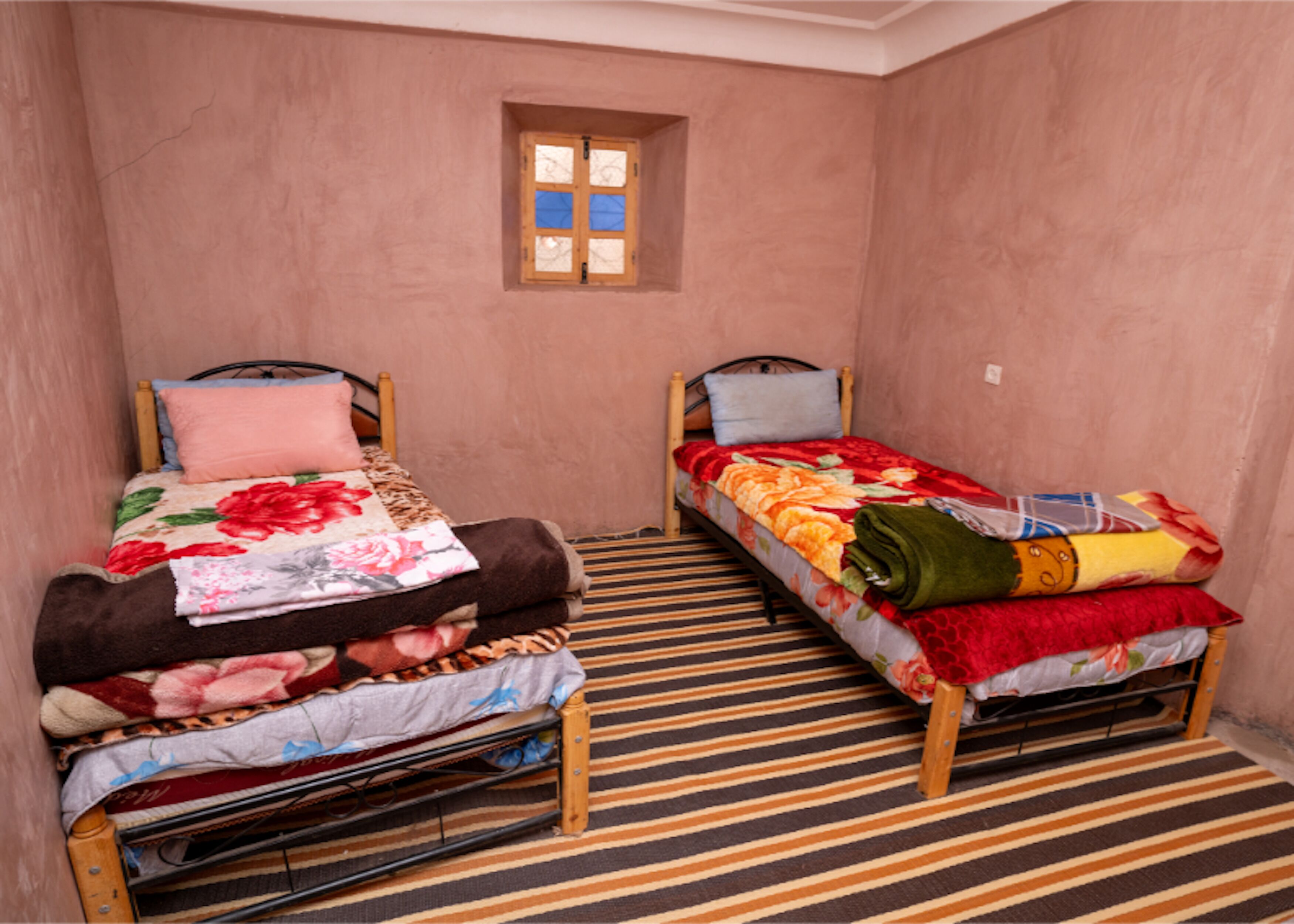 A small room with two single beds, a window, and a striped floor.