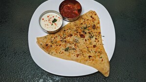 Un triángulo de pan plano con hierbas y una salsa blanca con especias rojas, sobre un plato blanco.