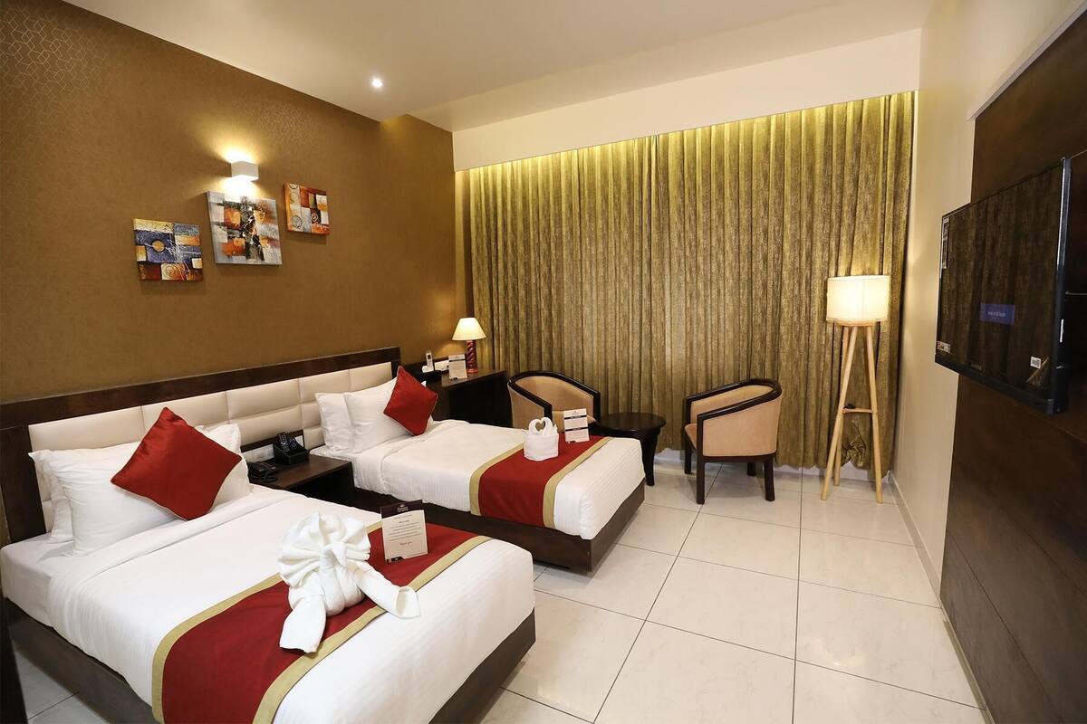 A hotel room with two beds, a desk, a chair, a TV, and artwork on the walls.