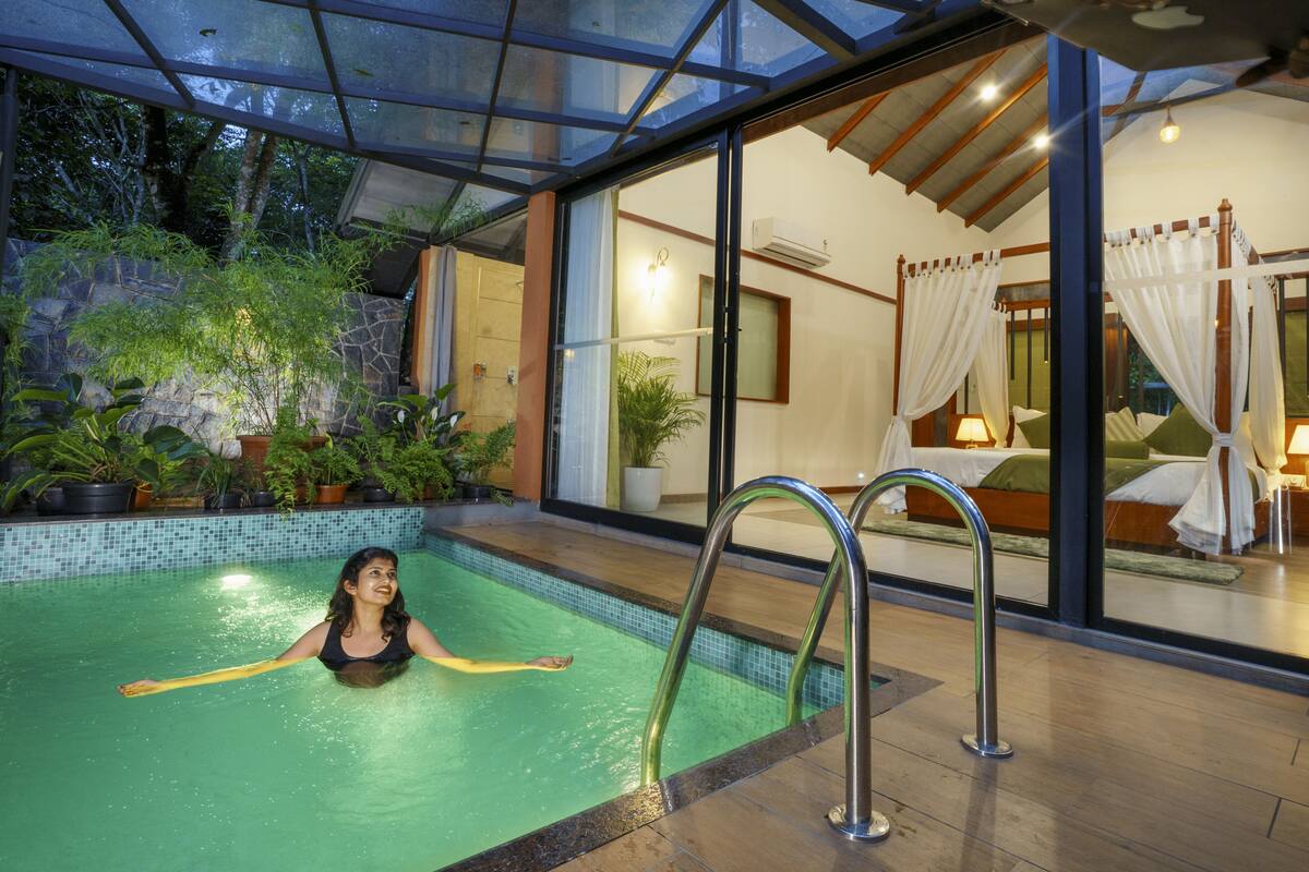 A swimming pool with a glass ceiling, surrounded by potted plants and a bed with a canopy.